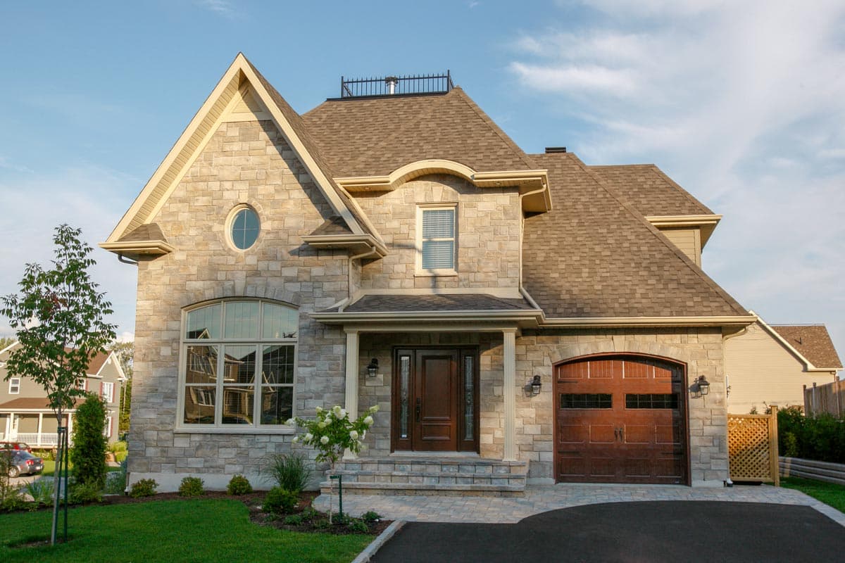 House plan exterior. Two-story, stone facade with gables, a front entry porch, and an attached garage with carriage-style door.