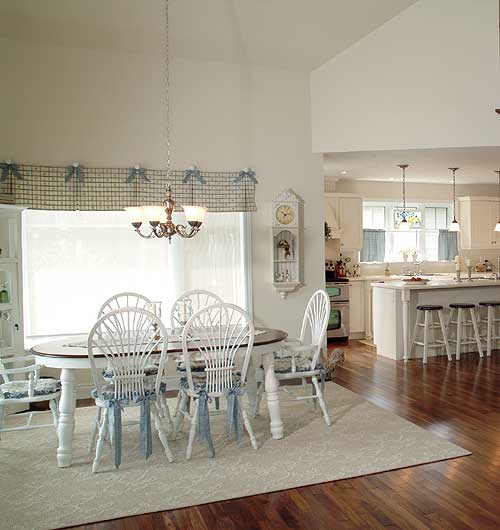 Open concept dining and kitchen area with vaulted ceilings, a breakfast bar, and white furniture.