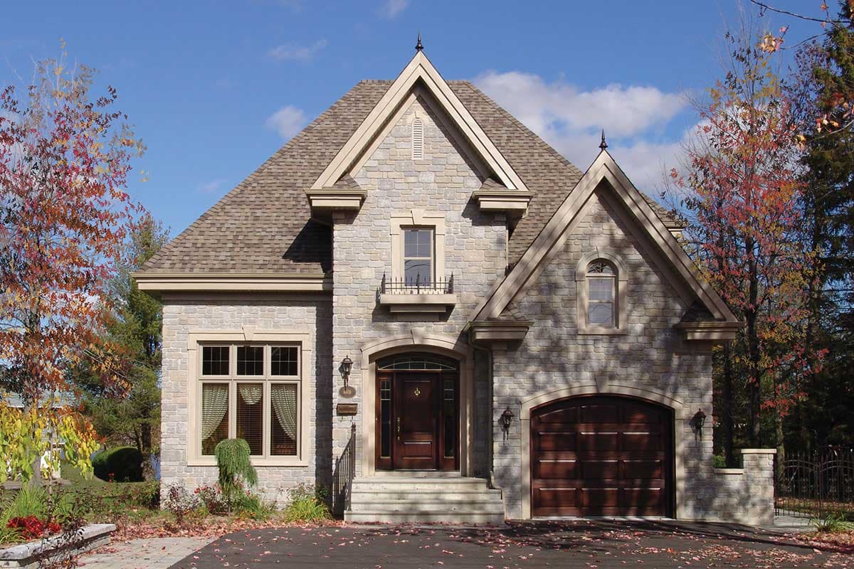 House plan exterior of a stone-clad two-story home with a steeply pitched roof, arched entryway, and attached garage with arched door.