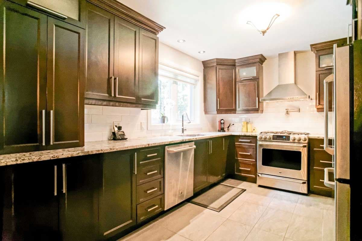 Corner kitchen with dark wood cabinets, granite countertops, stainless steel appliances, and subway tile backsplash.