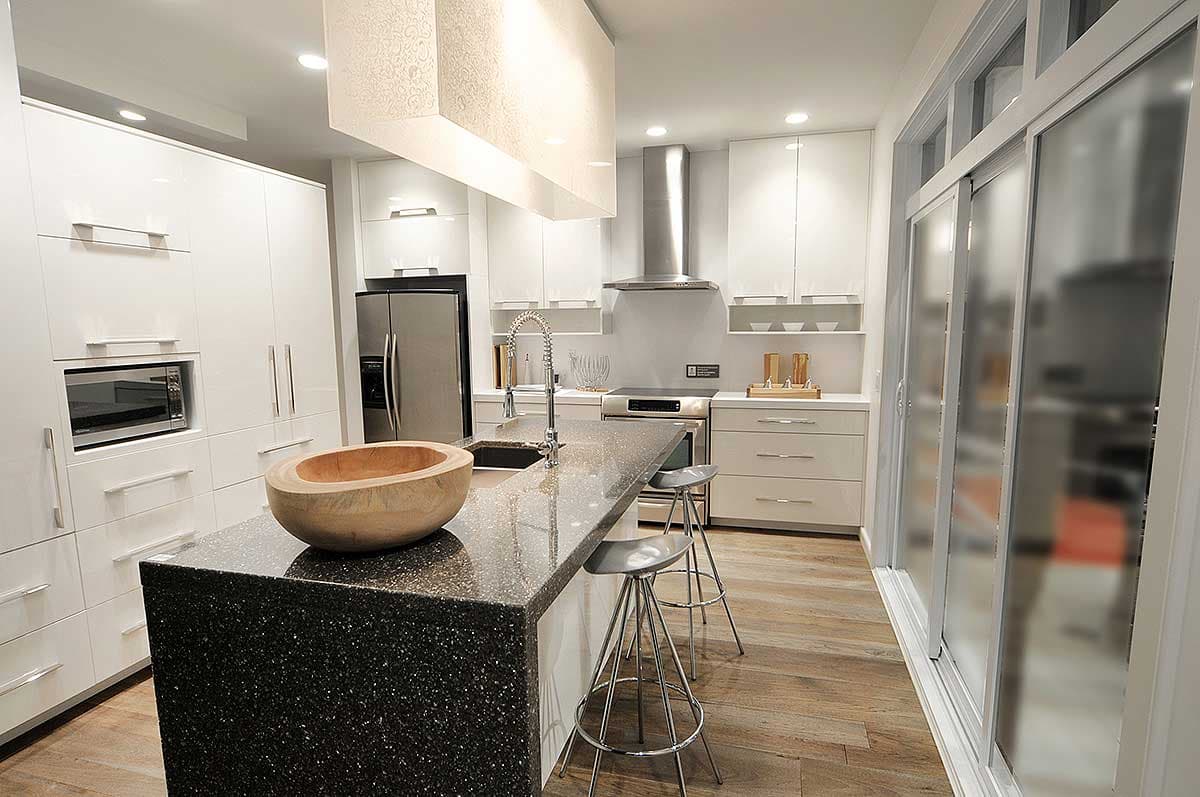 Modern kitchen with white high-gloss cabinetry, a granite island with sink, stainless steel appliances, and frosted sliding glass doors.