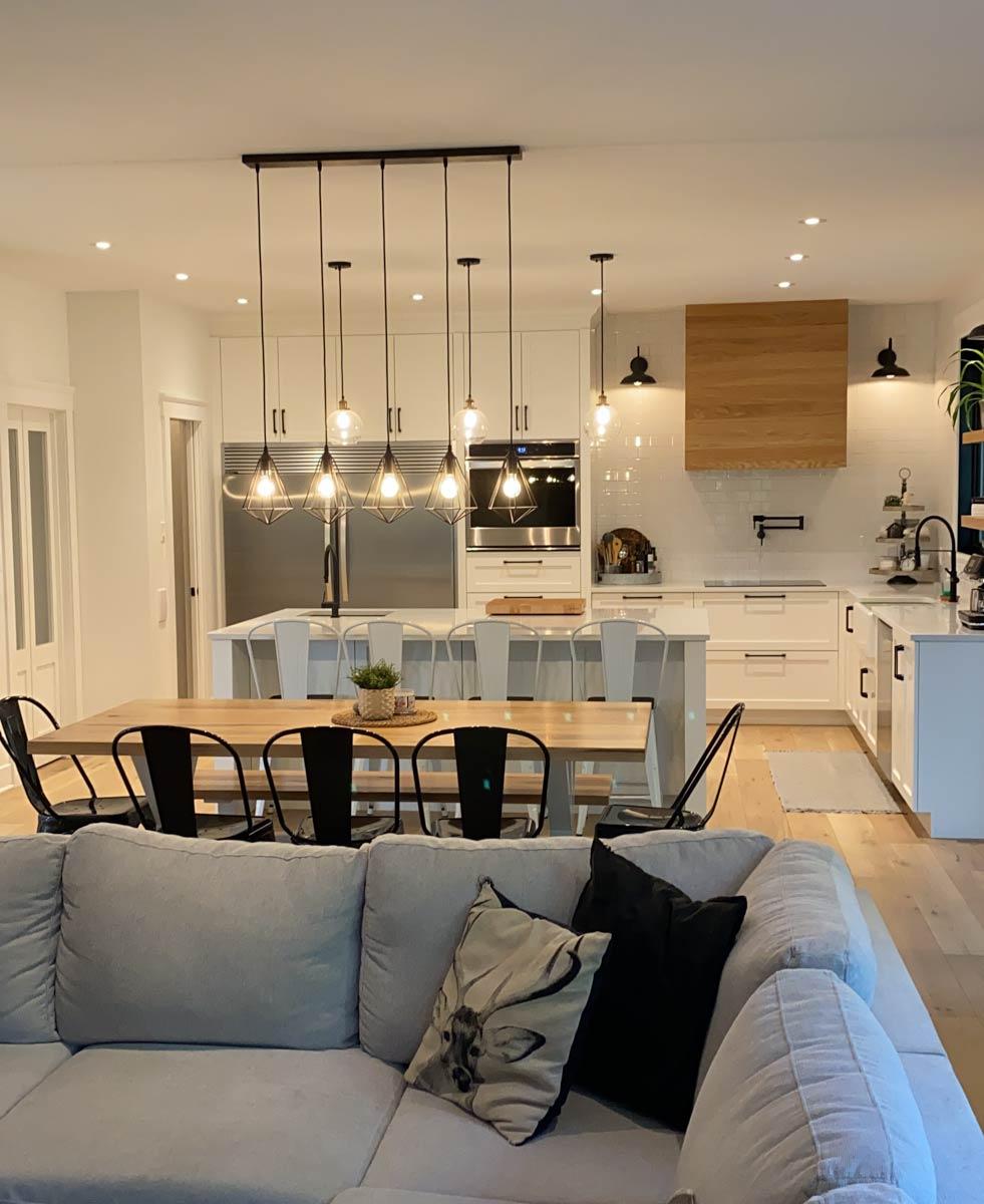 Modern open-concept kitchen with island, dining area, and living space. Features white cabinetry, stainless steel appliances, and pendant lighting.