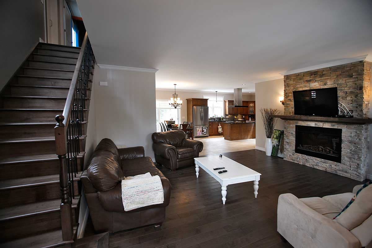 Open concept living area with stairs, stone fireplace, and kitchen with island.