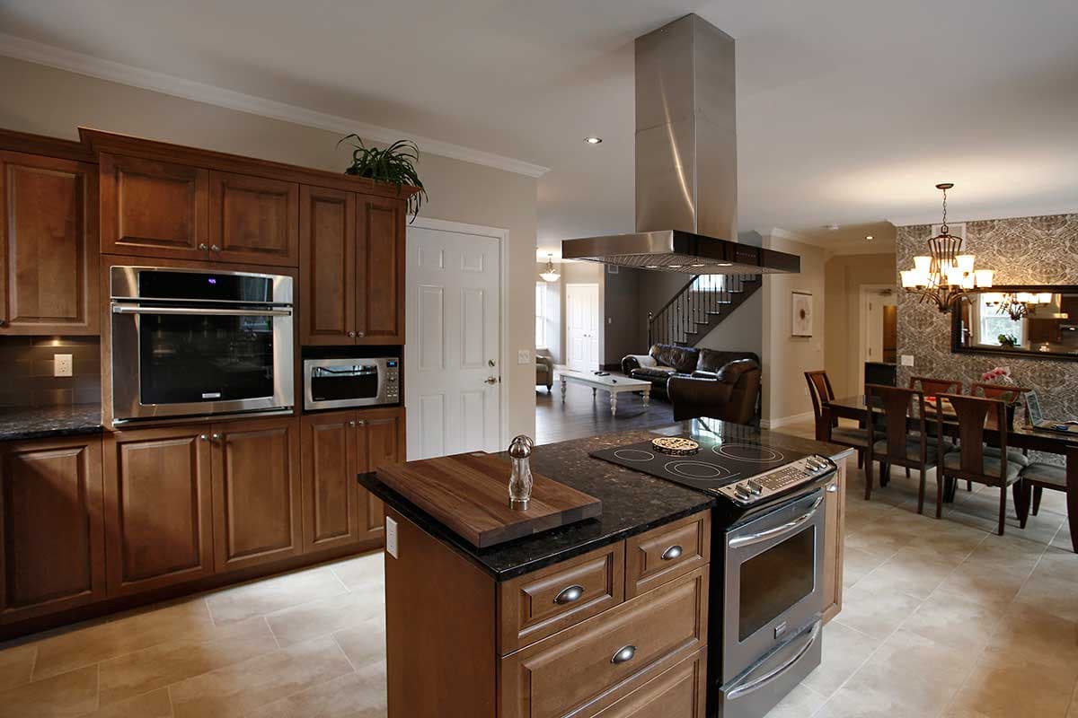 Kitchen with island, stainless steel appliances, wood cabinetry, open to dining area and living room with staircase.