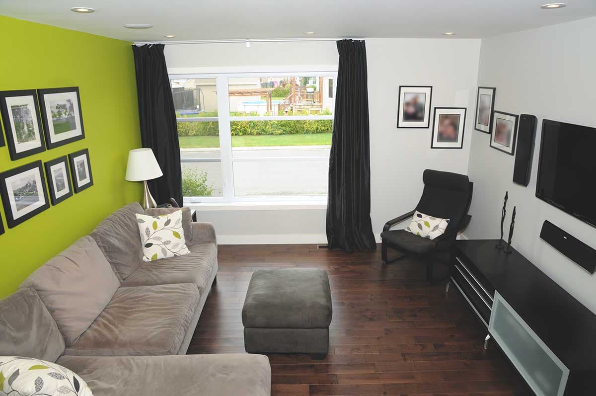 Living room with sectional sofa, accent wall, large window overlooking backyard, and media console.