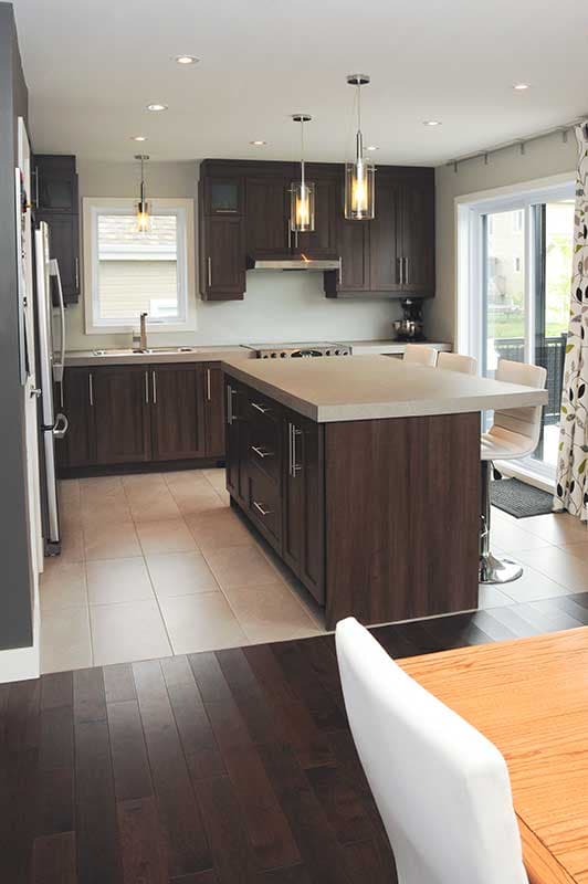 Modern kitchen with dark wood cabinetry, large island with seating, pendant lights, and stainless steel appliances.