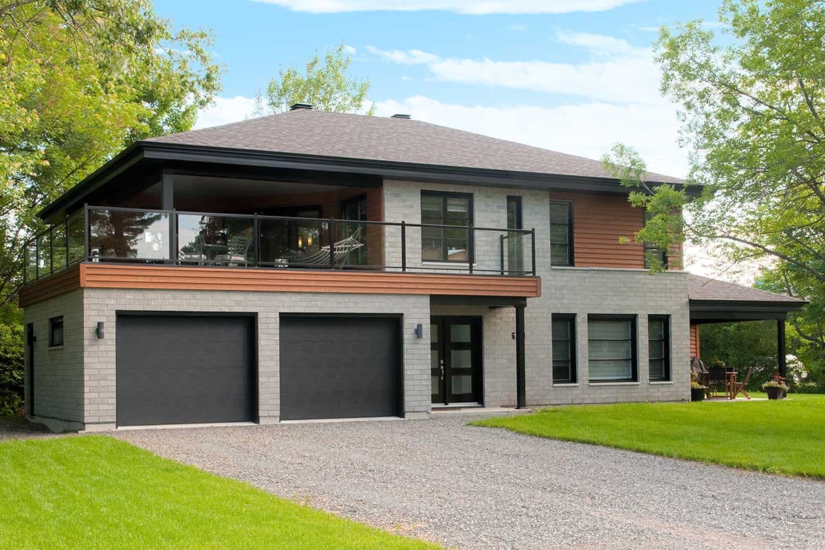 Modern house plan exterior with two-car garage, upper-level balcony with glass railing, and mixed-material facade.