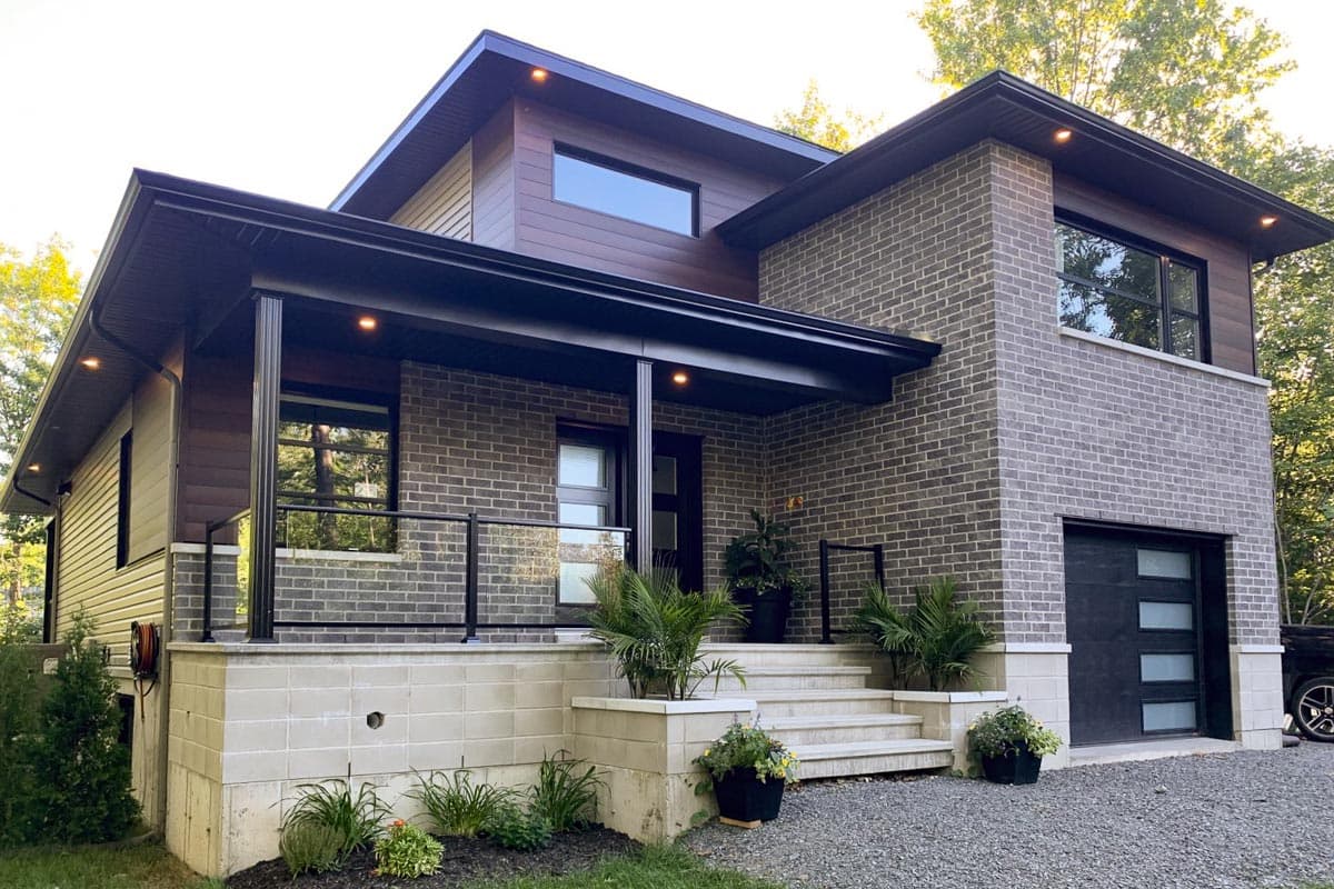 Modern two-story house plan with brick exterior, cantilevered second story, flat roof, and attached garage with glass panels.