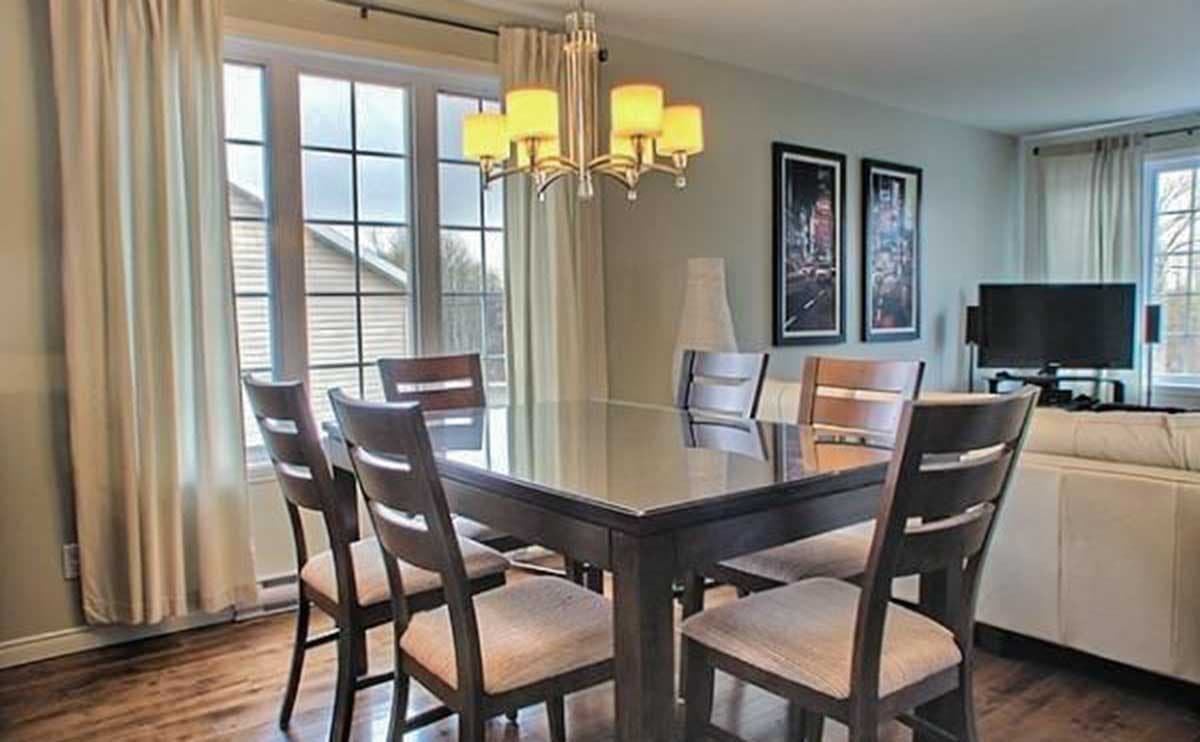 Dining room with dark wood table and chairs, large grid windows, and decorative chandelier.