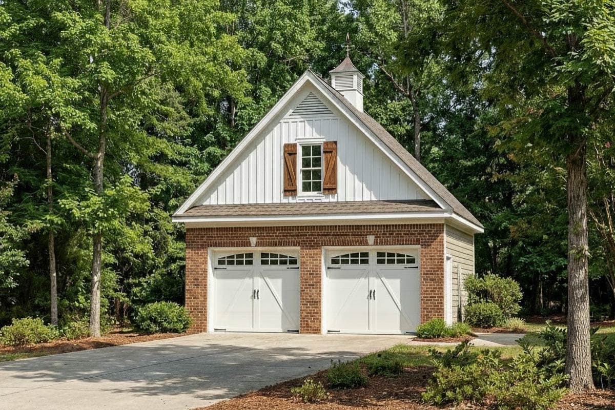 Garage plan exterior with two white garage doors, brick base, vertical siding, gable dormer, and cupola.