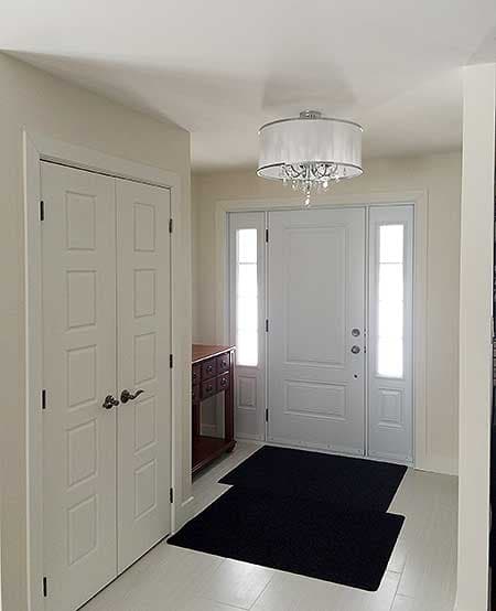 Interior view of a foyer with a double door closet, a wood console table, and a white front door with sidelights.