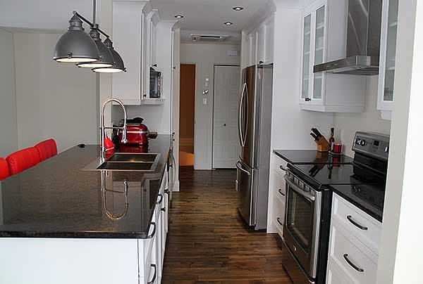Kitchen interior with dark granite countertops, stainless steel appliances, white cabinetry, and pendant lighting.