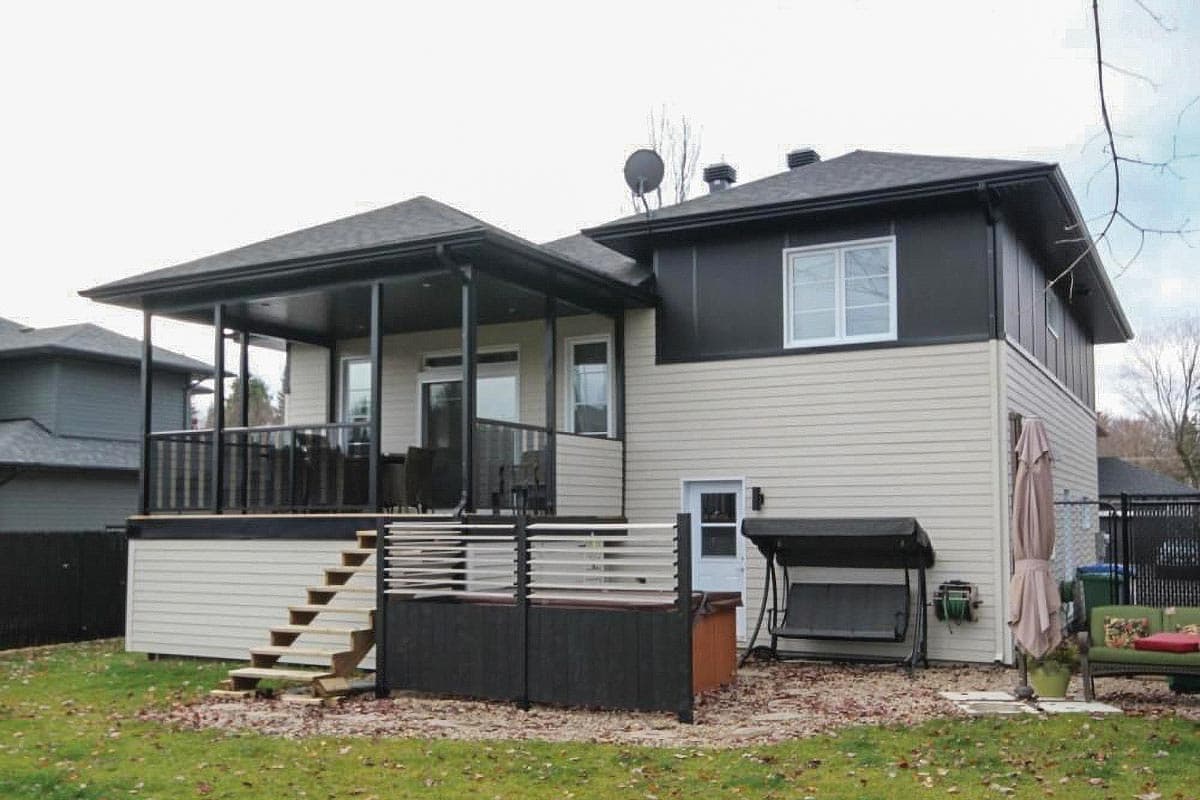 Two-story house exterior with covered porch, deck, side stairs, and dark contrasting upper story.