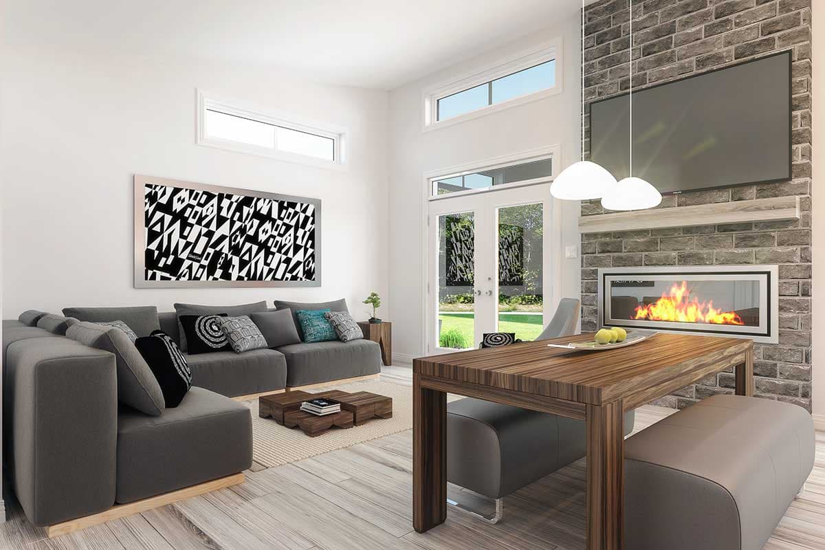 Modern living room with a gray sectional sofa, abstract art, and a brick fireplace with a lit fire and TV mounted above. A dining table is also present.
