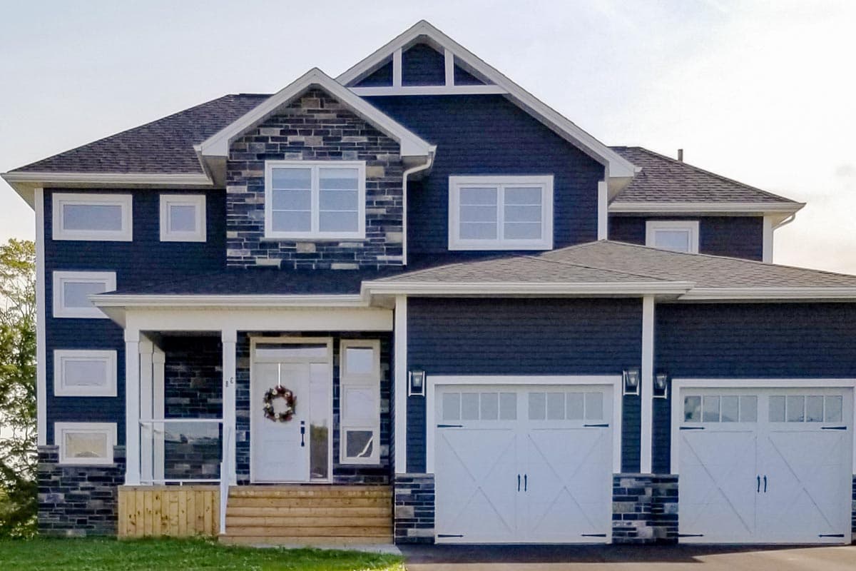 House plan exterior. Two-story home with a gabled roof, stone accents, and a front porch. Features an attached two-car garage.