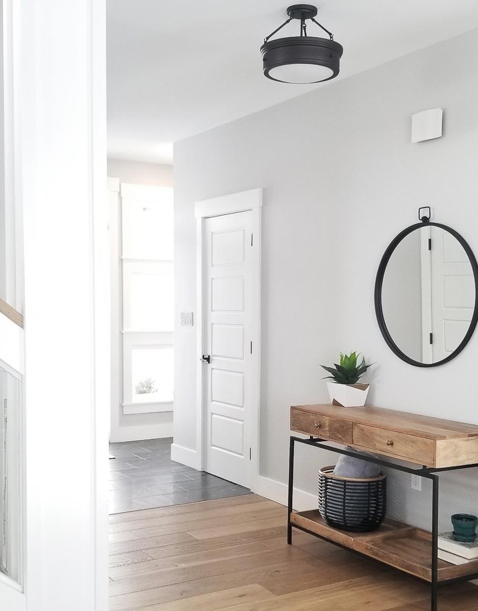 Interior hallway with natural wood flooring, a console table, a round mirror, and a flush-mount ceiling light.