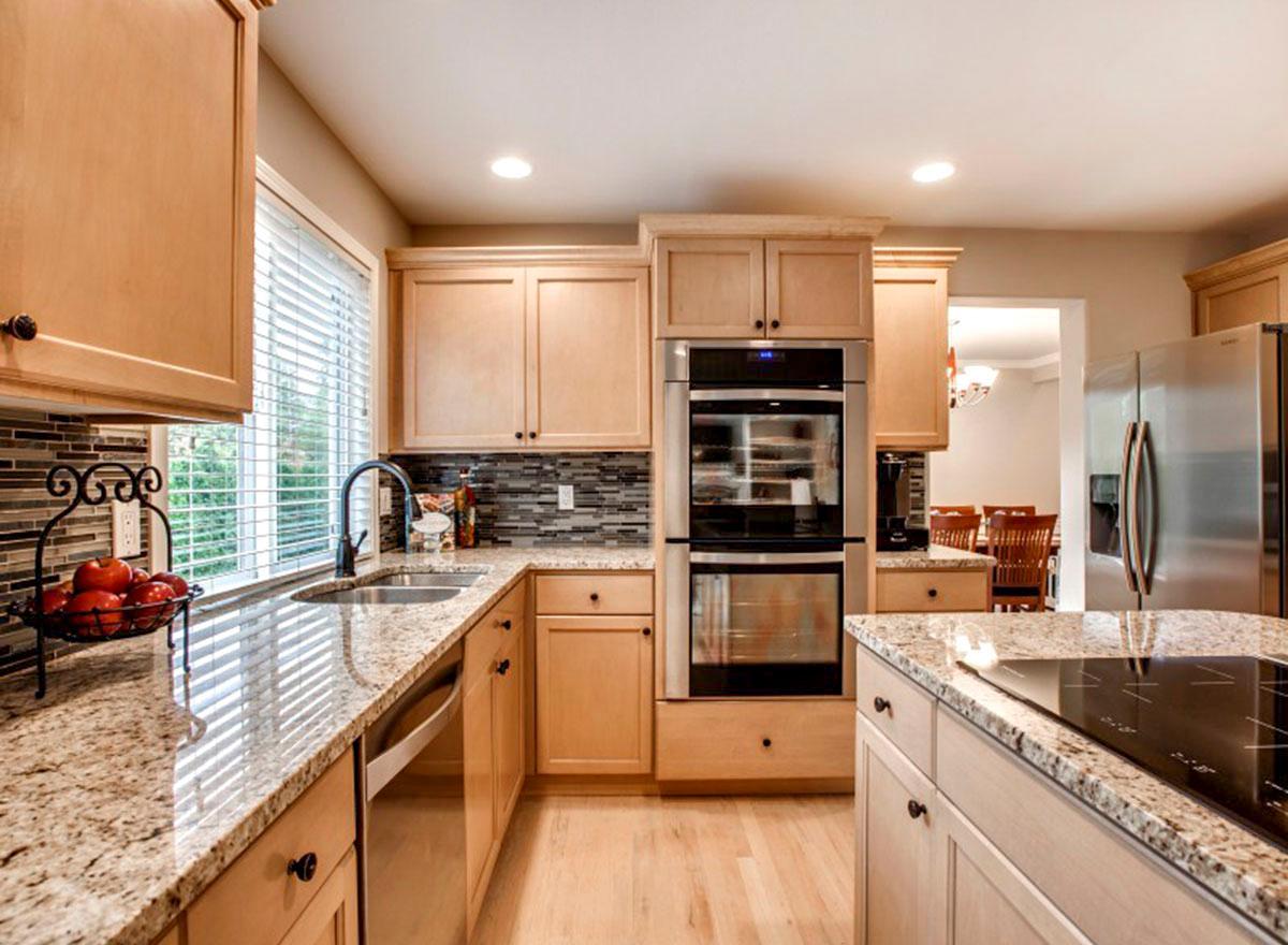 Kitchen with light wood cabinets, granite countertops, stainless steel double ovens, and a large island with a cooktop.