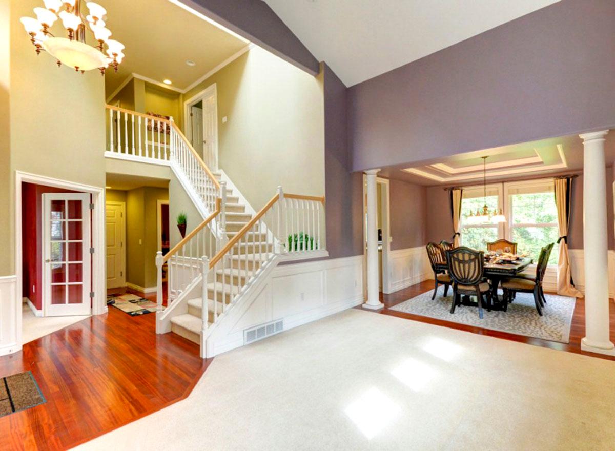 Foyer with grand staircase and adjacent dining area with coffered ceiling and large windows.
