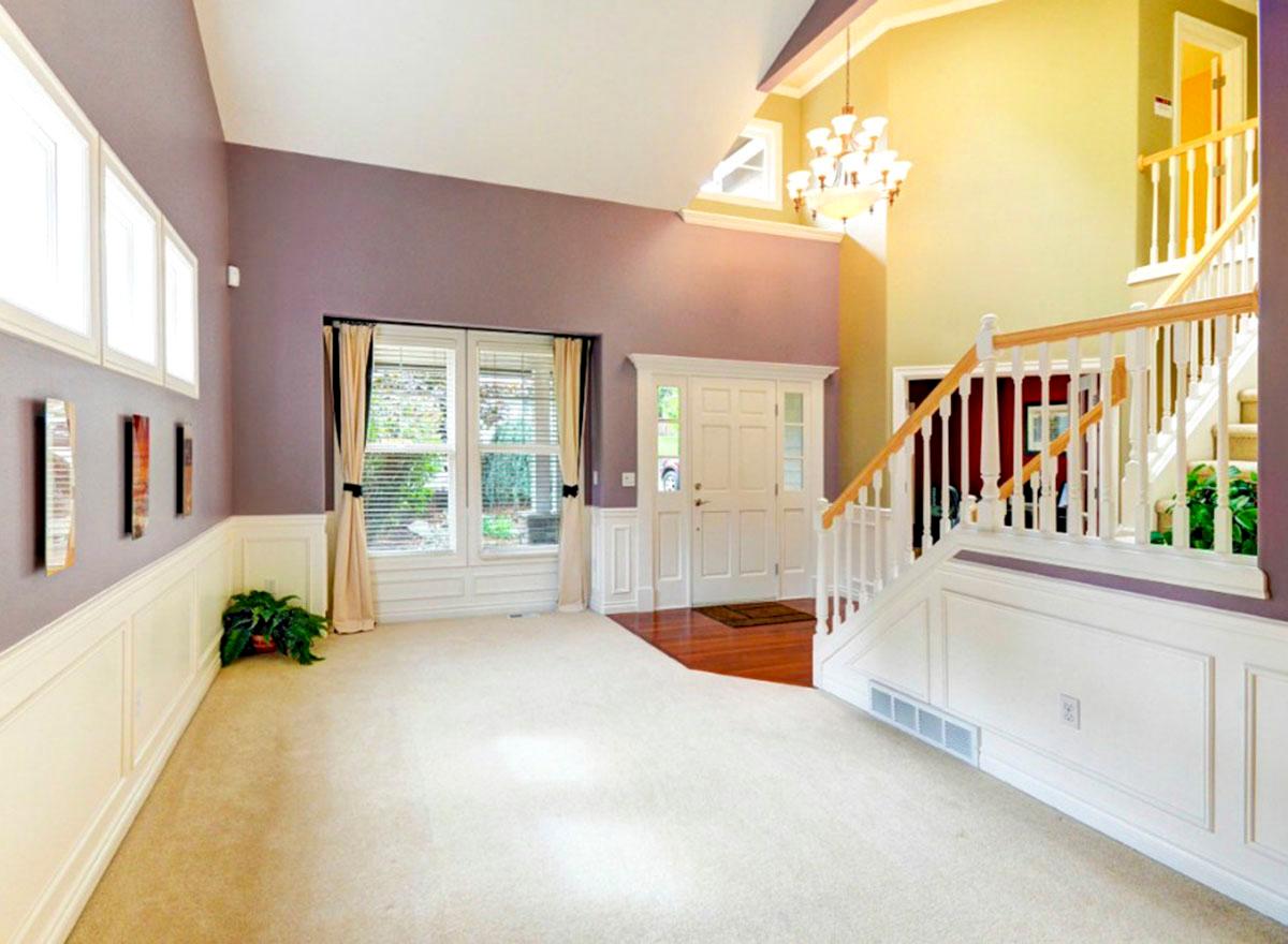 Interior view of a double-door entry with a cathedral ceiling, two-story staircase, wainscoting, and large windows.