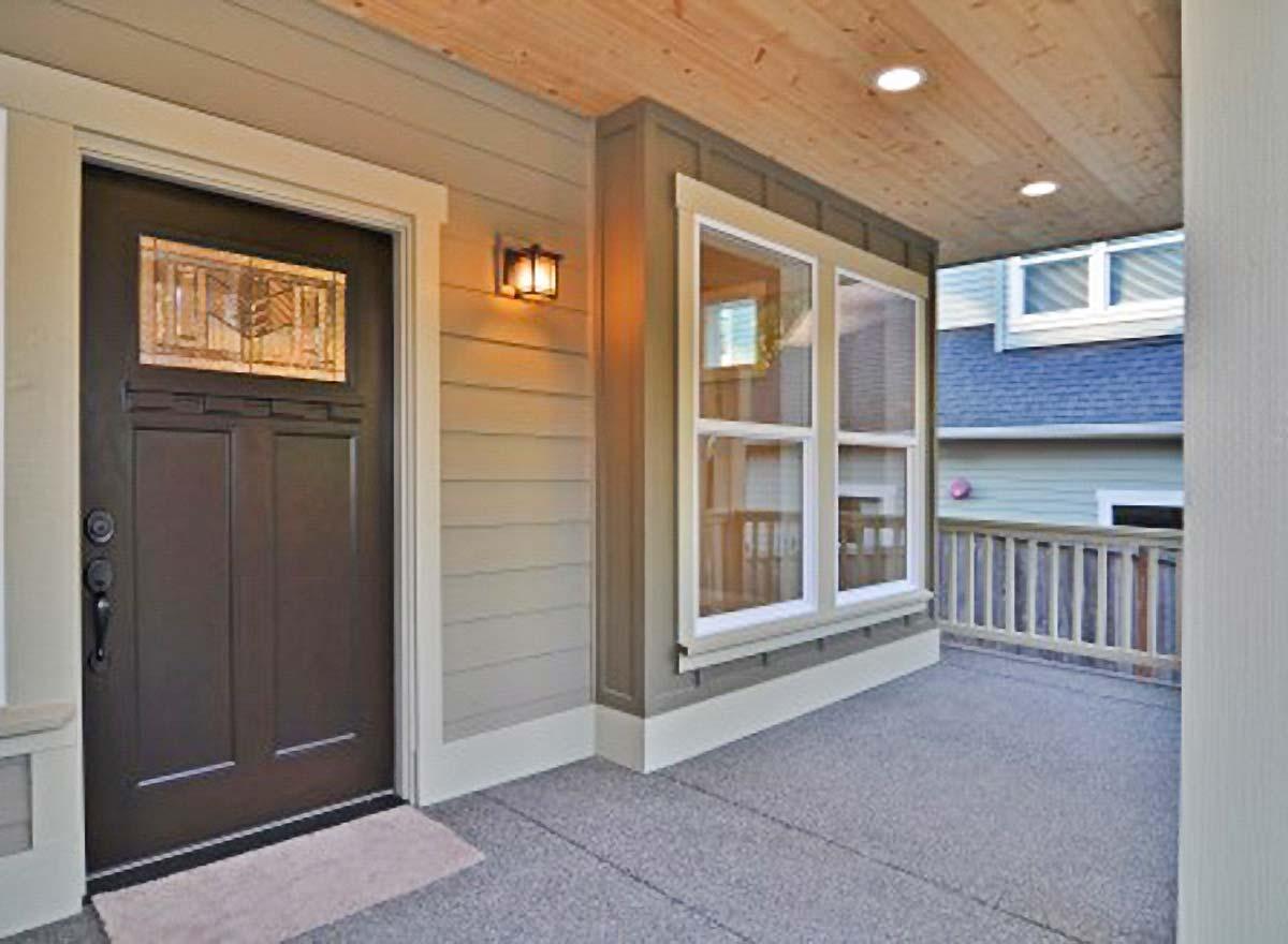 House plan exterior showing a covered porch with wood-paneled ceiling, entry door with stained glass, and double-hung windows.