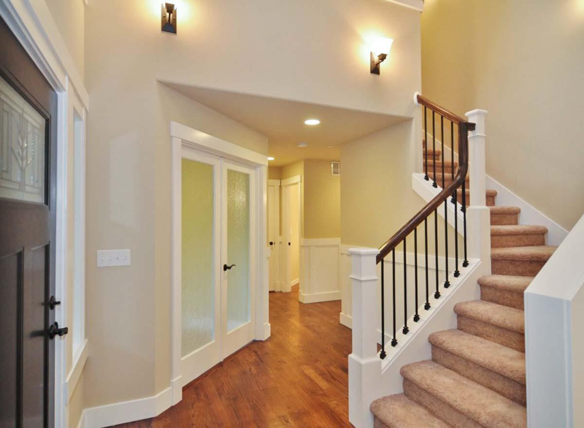 Interior view of a home entryway with a curved staircase, paneled wainscoting, and double frosted glass doors leading to a hallway.