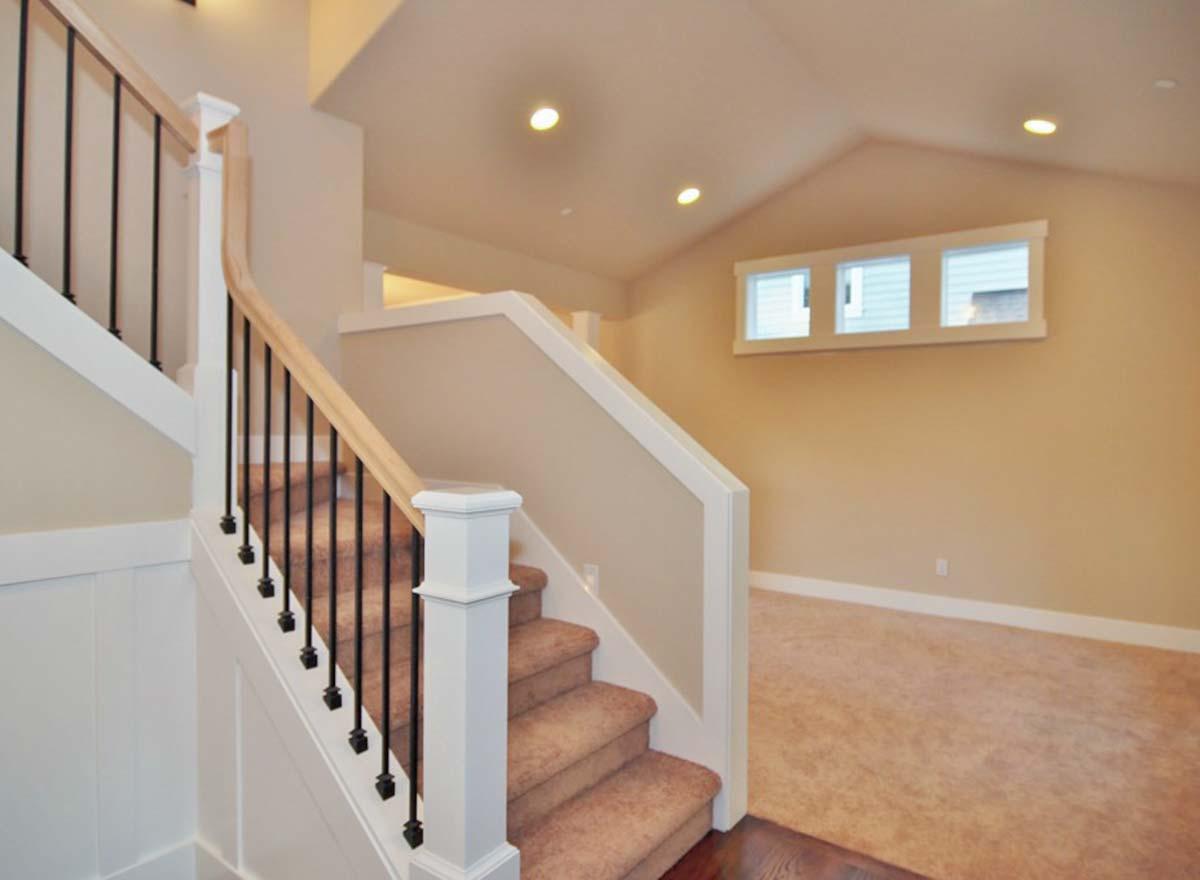 Interior view of a staircase with black metal balusters and a natural wood handrail, leading to a room with three clerestory windows.