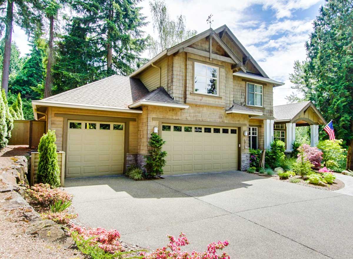 House plan exterior view of a two-story home with a three-car garage, wood shingle siding, gables, and a covered front porch.