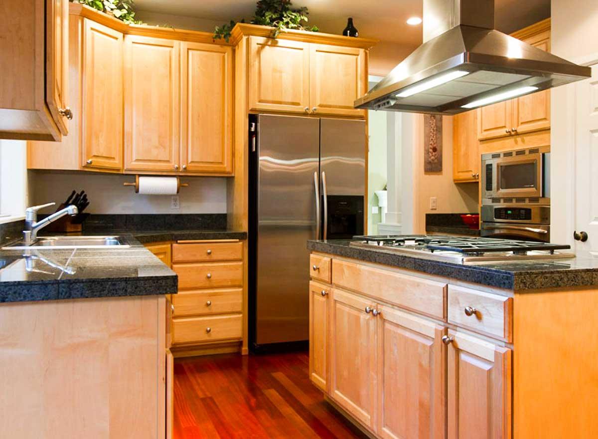 Kitchen with light wood cabinets, stainless steel refrigerator, granite countertops, and gas range with vent hood.