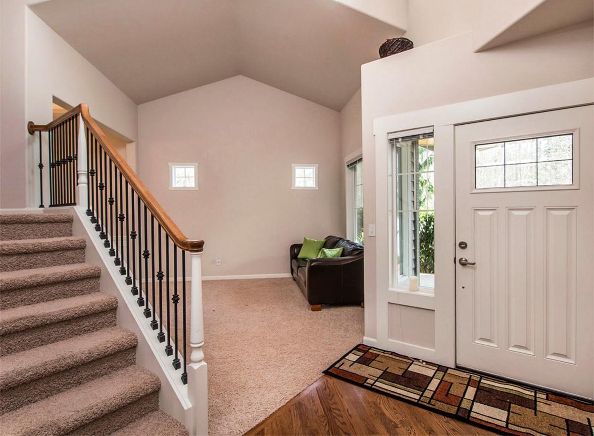 Interior view of entryway with carpeted stairs, vaulted ceiling, leather sofa, and glass-paneled front door.