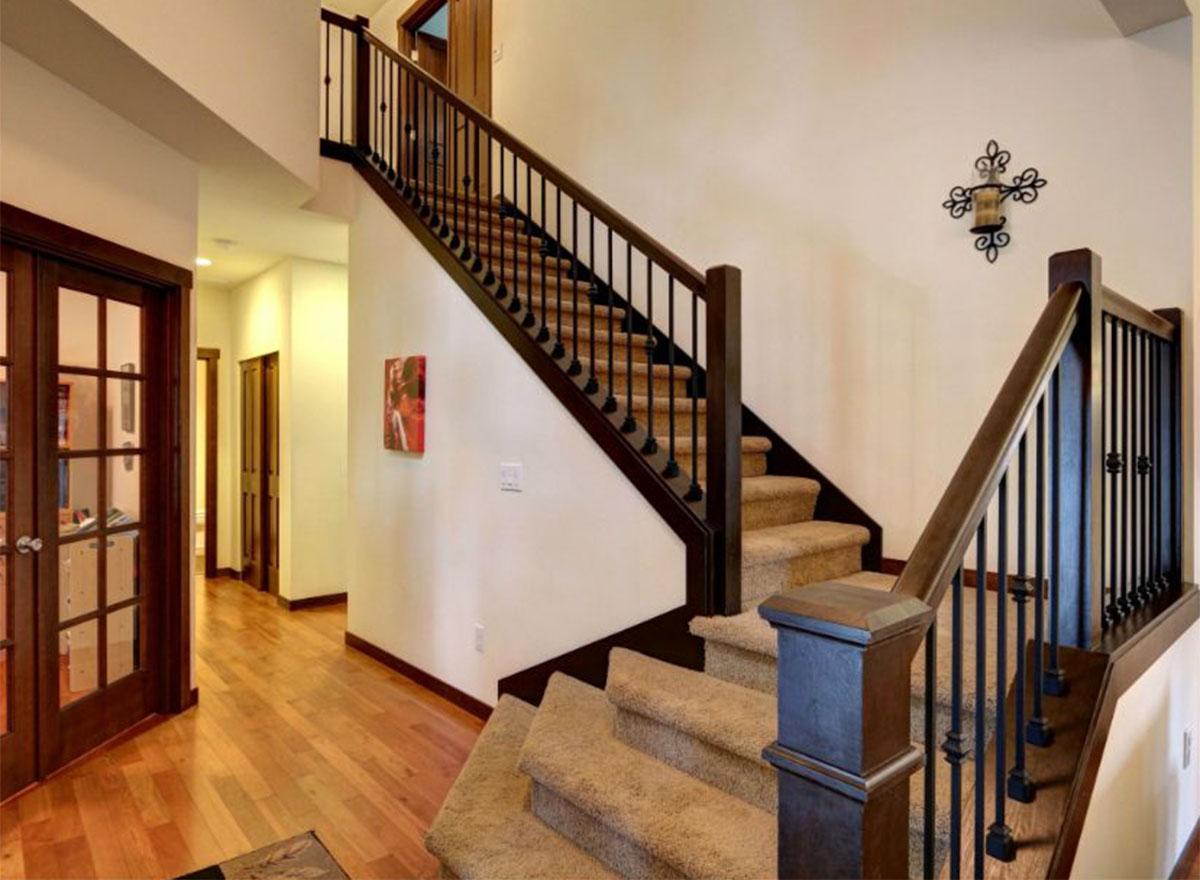 Interior view of a house with a carpeted staircase featuring dark wood banisters and spindles, wood flooring, and glass-paneled doors.