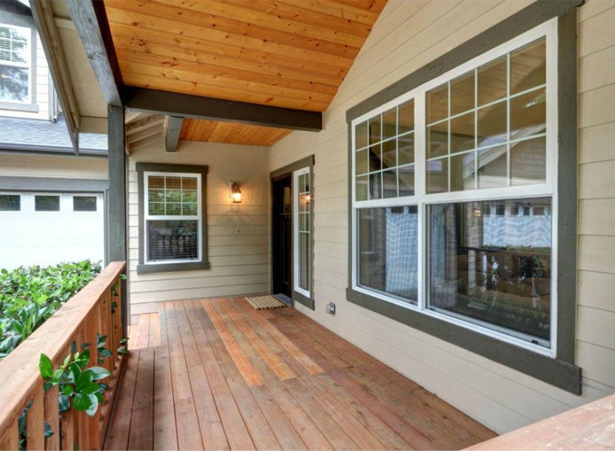 House plan exterior showing covered porch with wood deck, large windows, wood ceiling, and exposed beams.