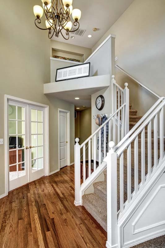 Interior view of a two-story home foyer with a staircase, glass-paneled doors, and hardwood flooring.