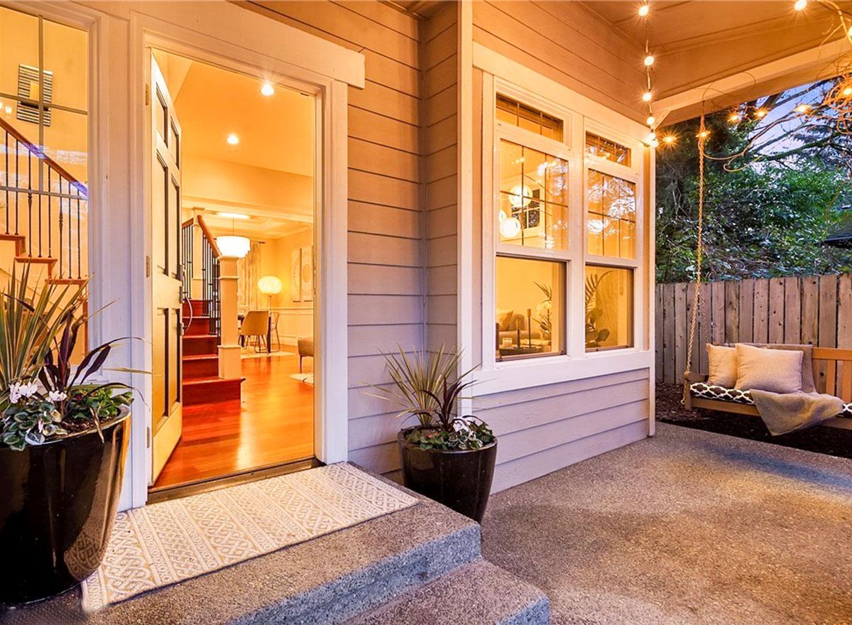 House plan exterior with open door showing staircase, porch with swing, and double-hung windows.