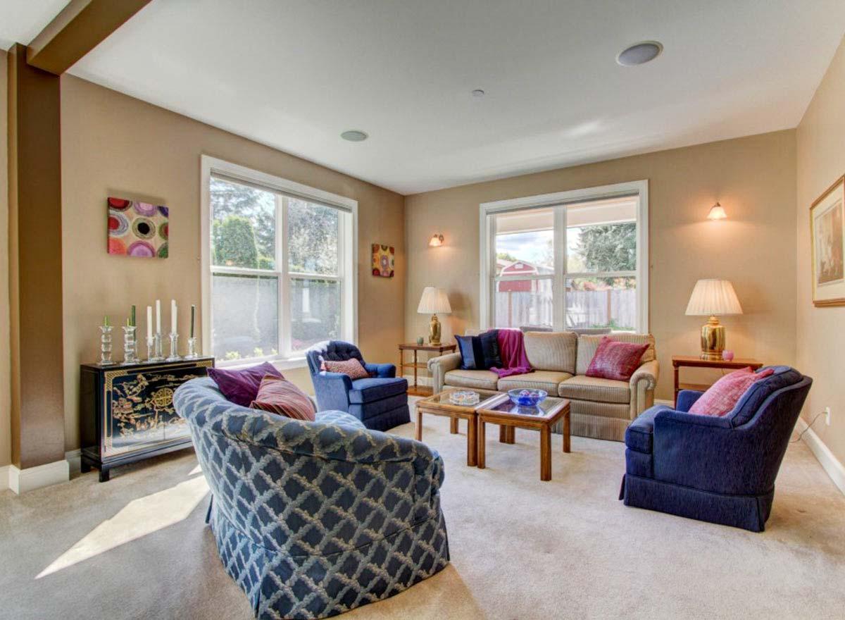 Living room with neutral carpet, two sofas, two armchairs, two coffee tables, and large windows.