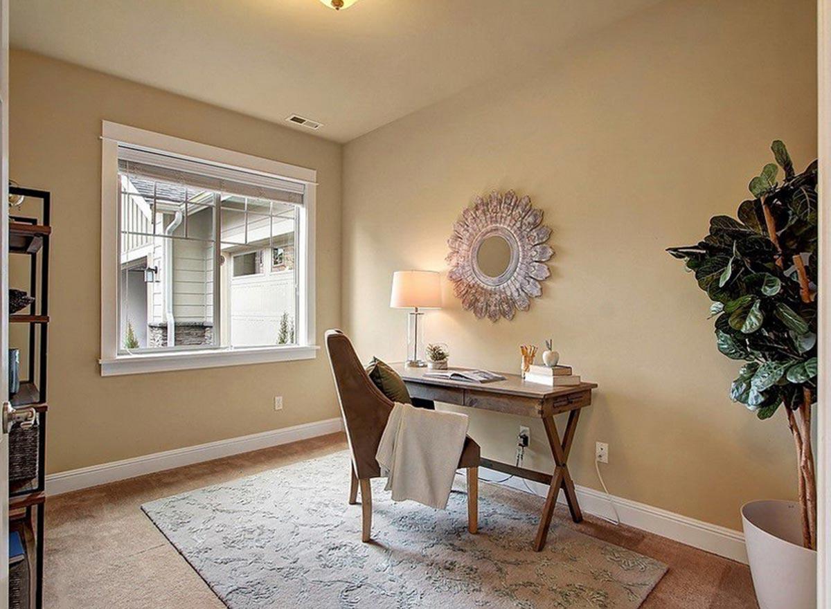 Office space with desk, chair, and window overlooking exterior. Features patterned rug and wall mirror.