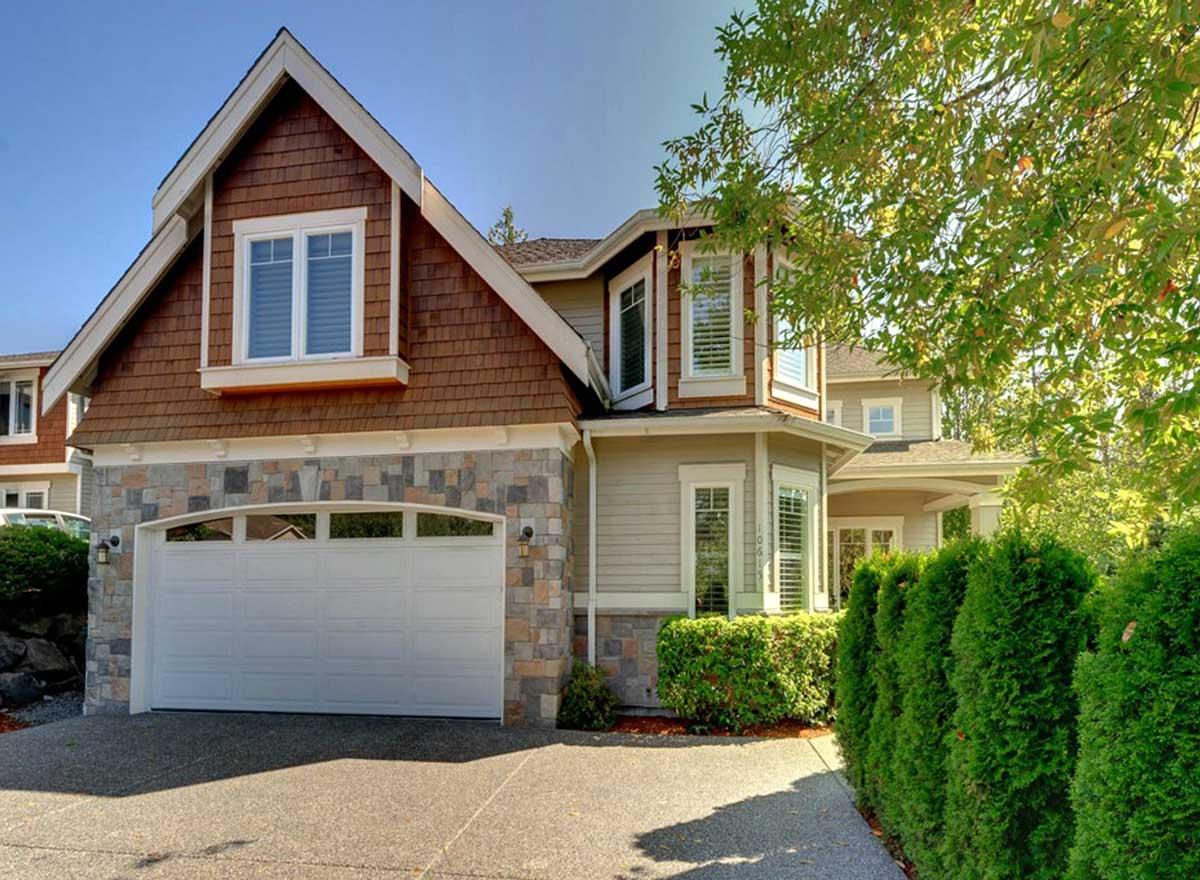 House plan exterior with stone and wood shingle facade, multi-level gables, bay windows, and a wide garage door.