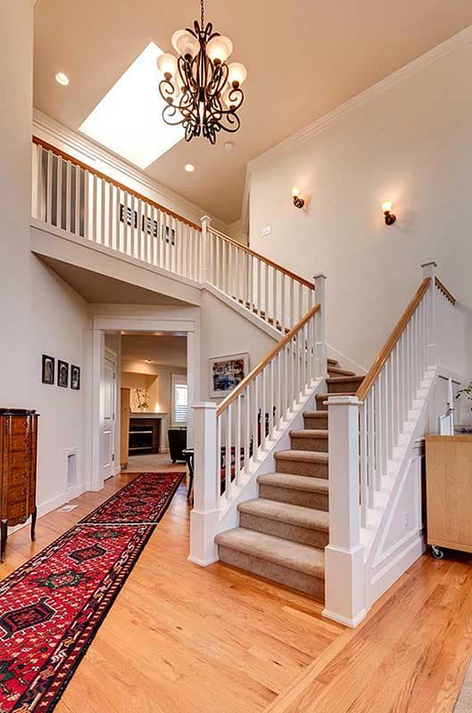 Interior view of a grand staircase with a skylight and ornate chandelier. White railings and wood flooring are visible.