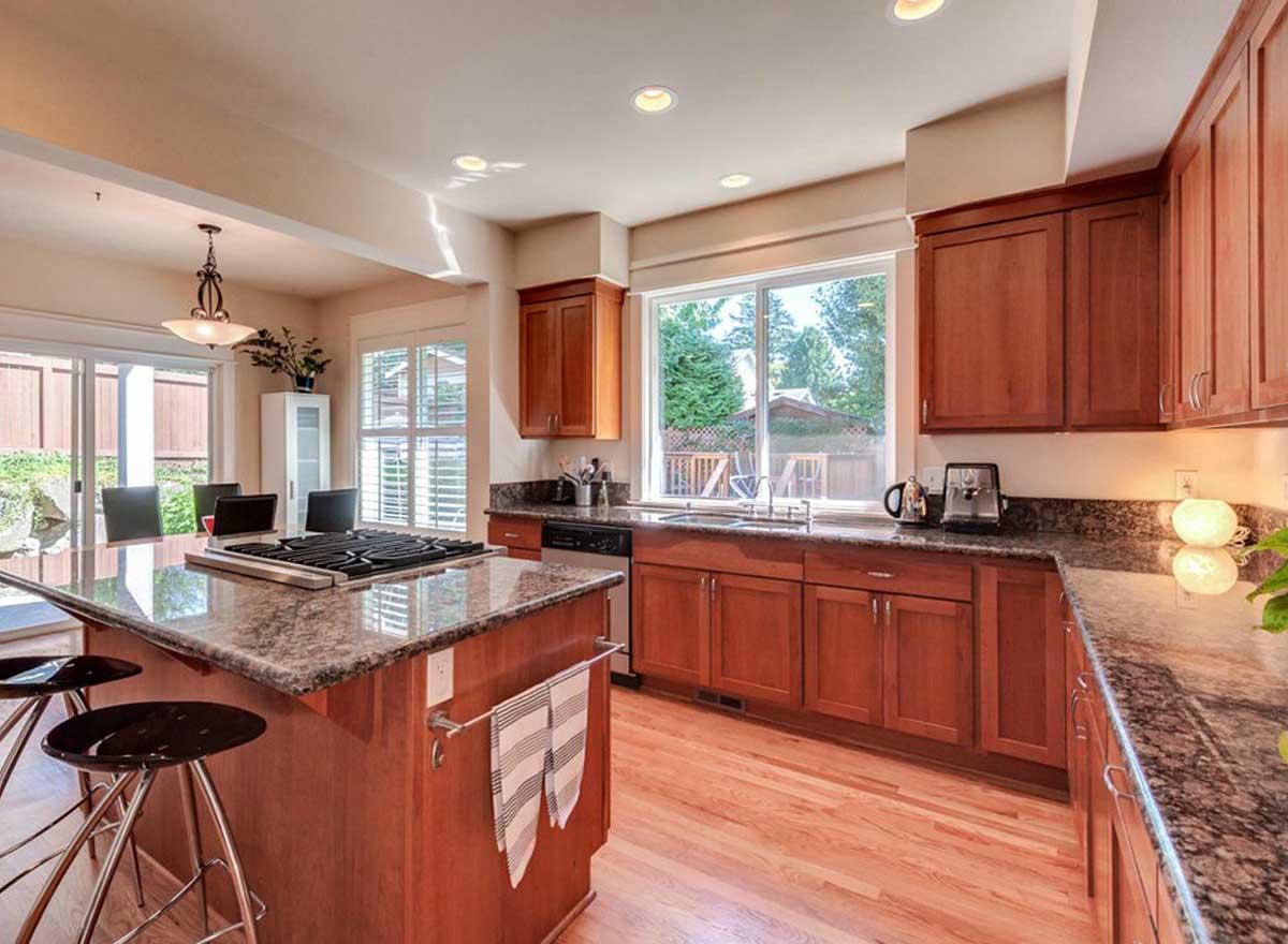 Kitchen with wooden cabinets, granite countertops, island with stovetop, and large window overlooking backyard.