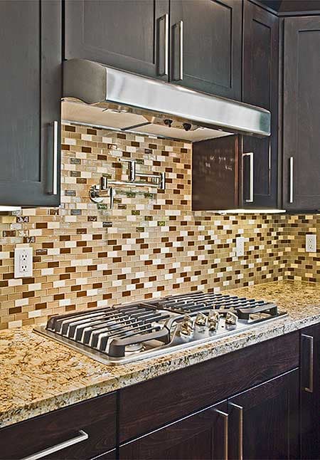Kitchen gas range with pot filler faucet on backsplash with mosaic tile, granite countertop, and dark wood cabinets.