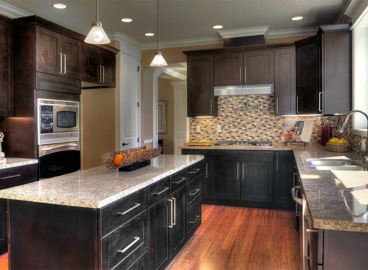 Kitchen with dark wood cabinets, granite countertops, island, mosaic tile backsplash, and stainless steel appliances.