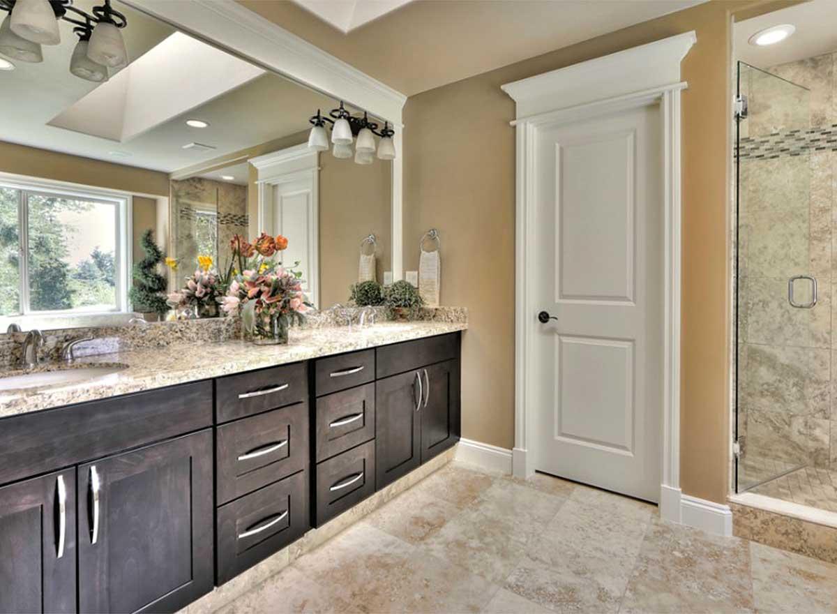 Bathroom interior with double vanity, granite countertops, dark wood cabinets, mirrored wall, and glass-enclosed shower.