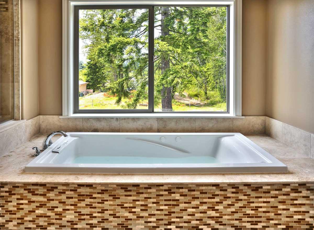 Jacuzzi tub with mosaic tile surround and a large window overlooking trees.