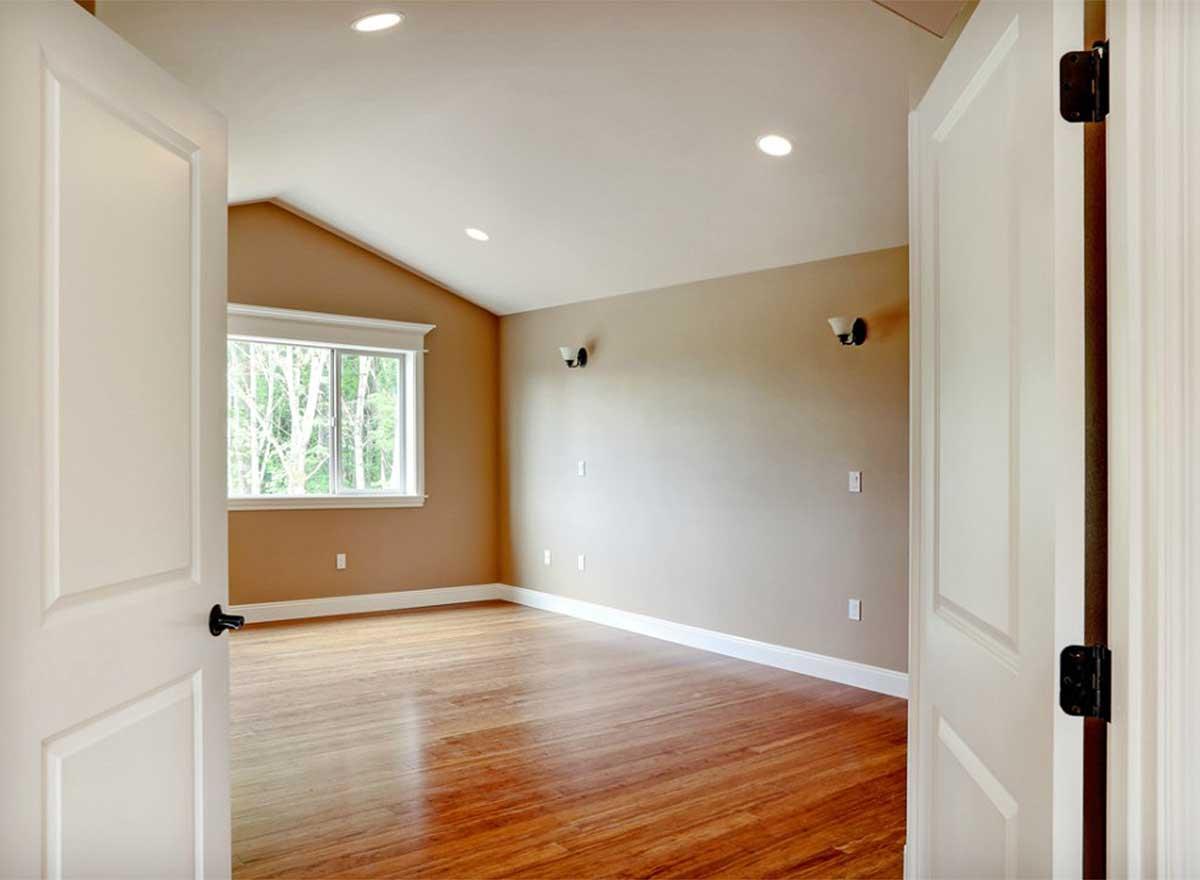 Interior view of an empty room with vaulted ceiling, hardwood floors, and a large window overlooking trees.