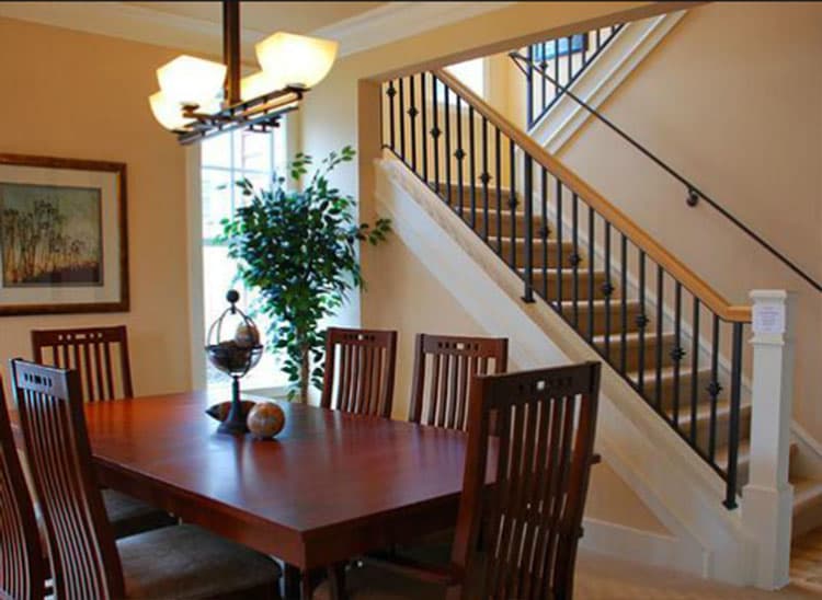 Dining area with wood table and chairs adjacent to a staircase with black balusters and wood handrail.