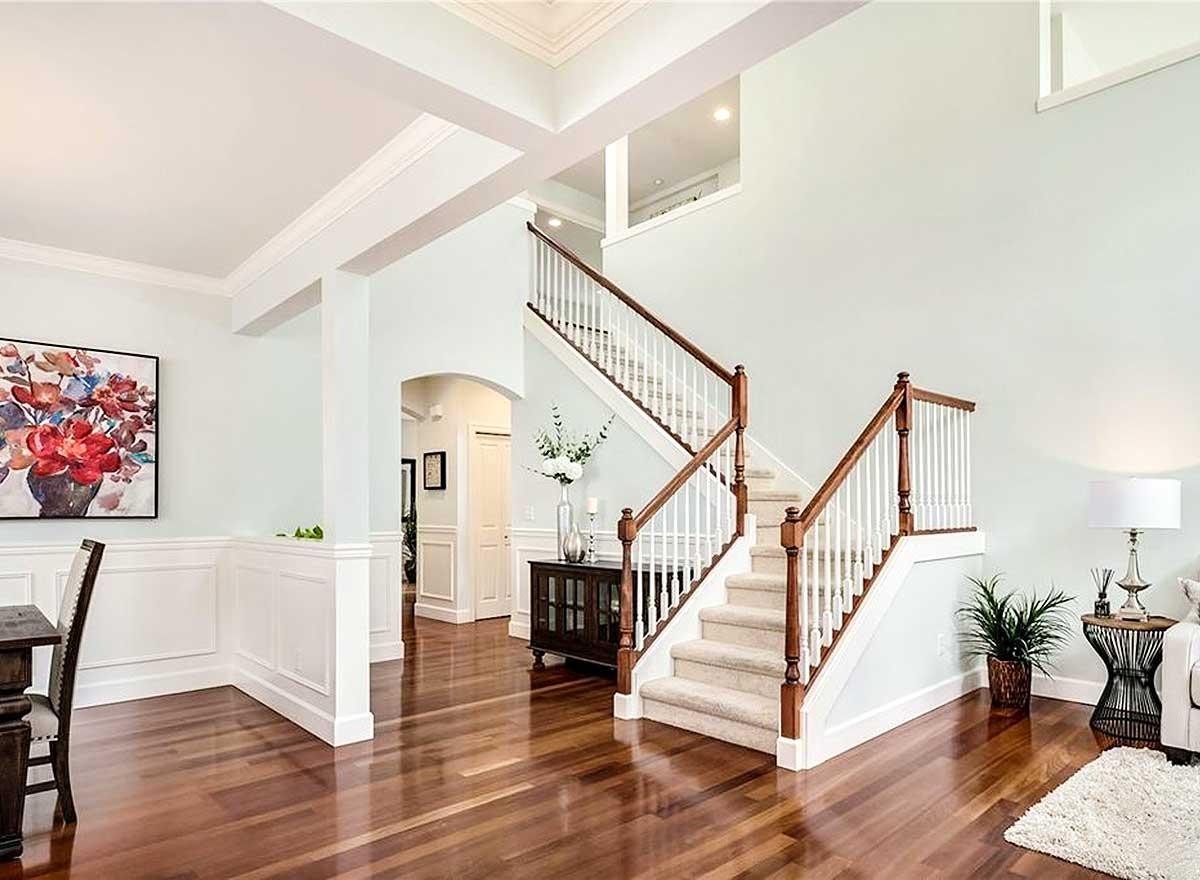 Foyer with dual staircase, coffered ceiling, wainscoting, and arched entryway to hallway. Hardwood floors.