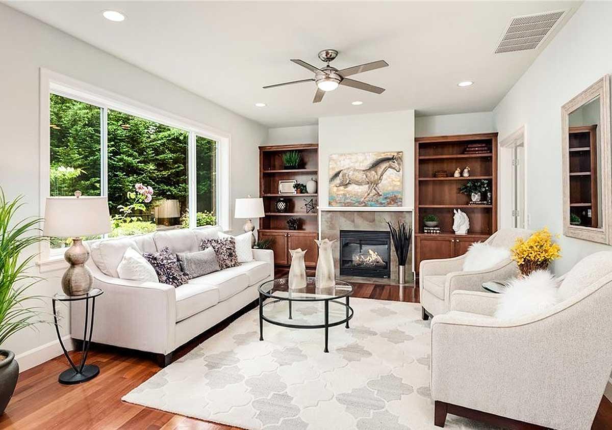 Living room with fireplace, built-in bookshelves, large window, and ceiling fan.