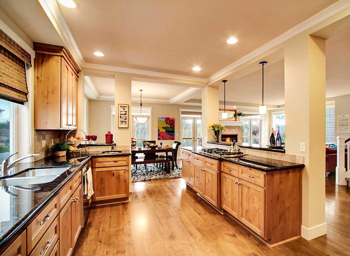 Kitchen with light wood cabinets, granite countertops, island, and view to dining area with fireplace.