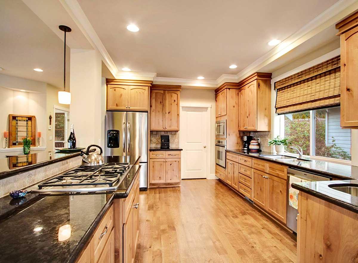 Kitchen with light wood cabinets, stainless steel appliances including a refrigerator and double ovens, granite countertops, and hardwood floors.