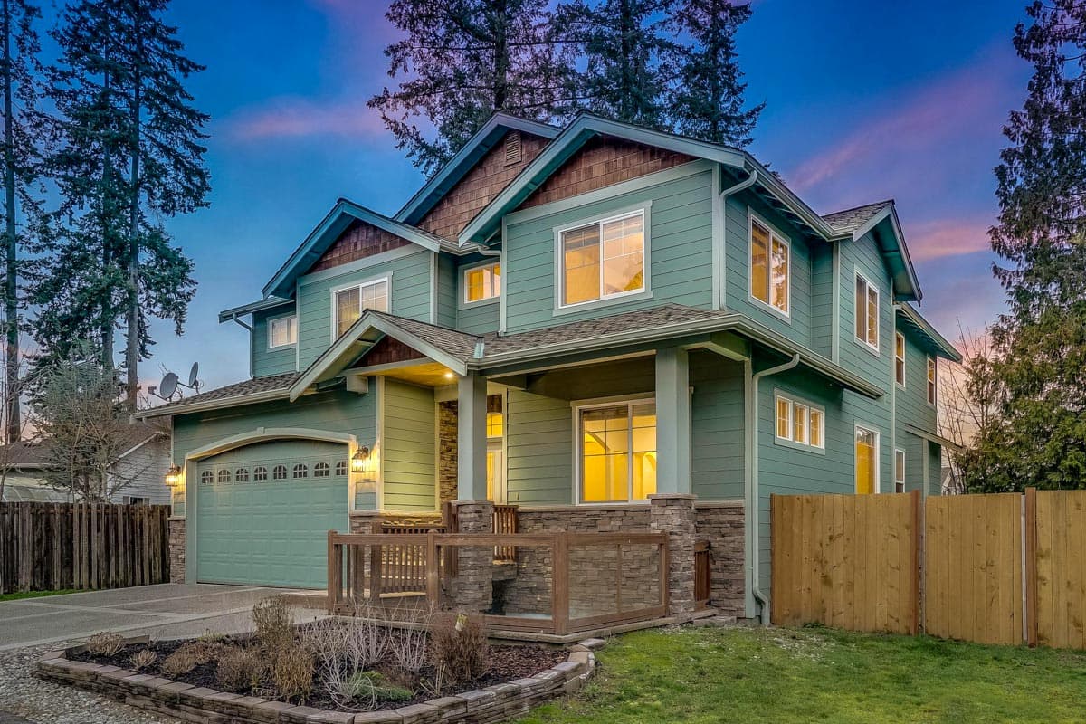 House plan exterior: two-story home with gabled roof, covered porch with stone base, and attached garage.