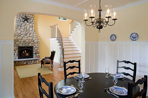 Interior view showing dining area with round table and living area with stone fireplace and curved staircase.